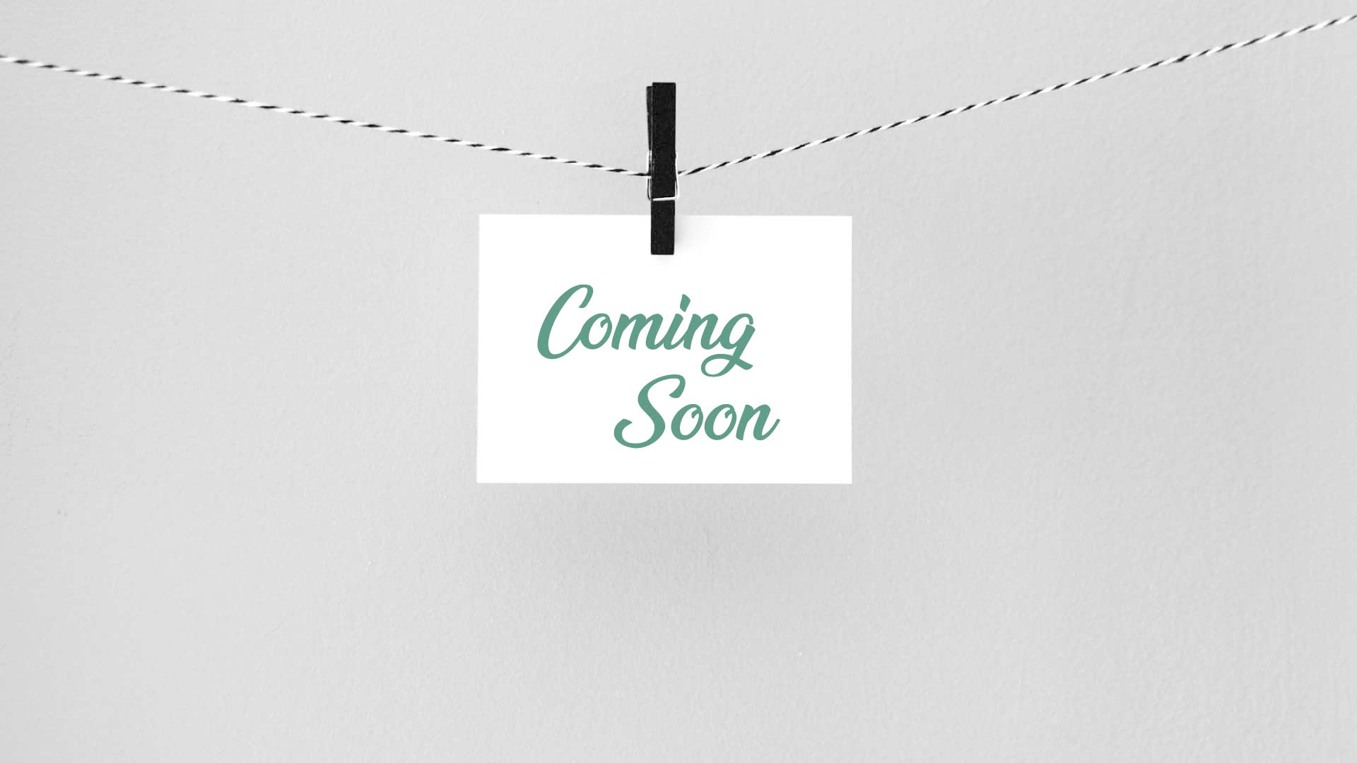 a coming soon sign hanging from a string with a clothespin